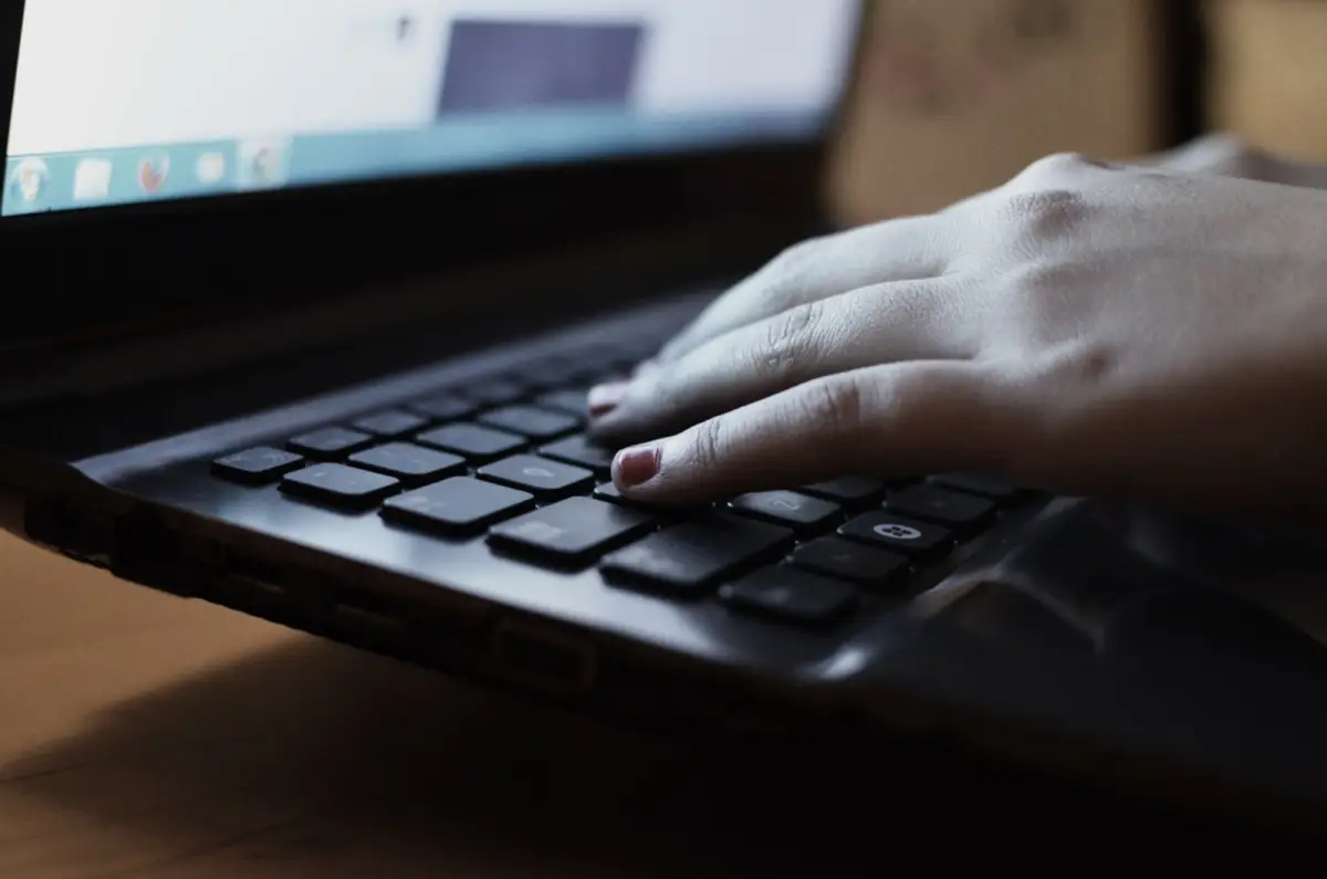Main tapant sur un clavier d'ordinateur portable face à un écran, pour répondre à des avis en ligne